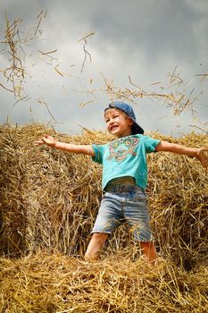 Schoolboy boy jumping and having fun on straw bales on summer day