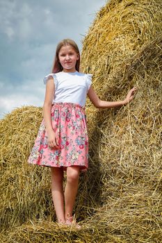 Model Girl with long blonde hair in a pink dress climbed on large bales of straw on a hot summer day