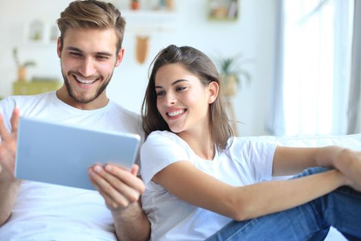 Young couple watching media content online in a tablet sitting on a sofa in the living room.