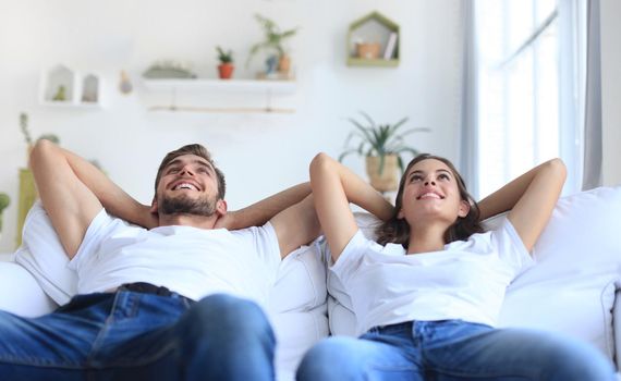 Smiling beautiful couple sitting on a sofa and dreaming about new home.