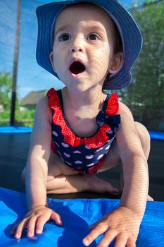 Eighteen months old girl in a dress is afraid to jump on the trampoline