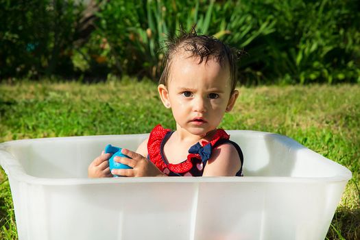 On a hot summer day a very serious girl playing with a rubber toy blue in a white bath