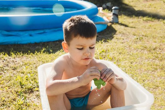 A little boy on a summer day playing with a toy in a white bath