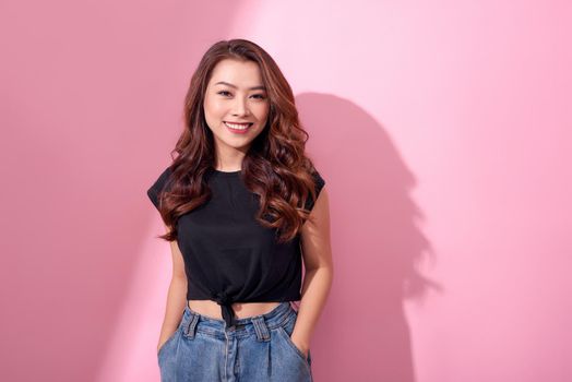 beautiful portrait Asian cheerful young girl poses in casual clothes with beaming smile standing isolated on pink background