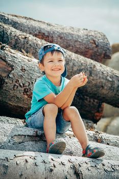 Preschool boy in a baseball cap sits on a log and laughs merrily