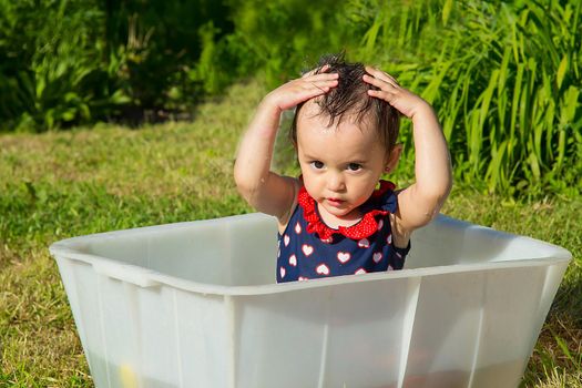 One and a half year old baby herself washes her head on the street on a hot day