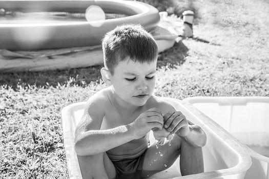 Black and white picture sad little boy sitting in the tub