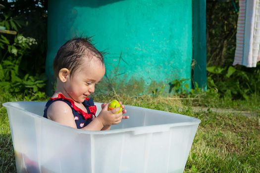 A little girl in a swimsuit sits in a white bath and plays with a yellow duckling