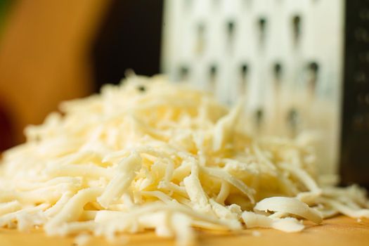 Picture of metal kitchen grater with oval holes on it on the kitchen table with cheese