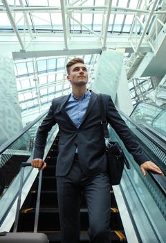 Businessman at the airport going down the escalator.