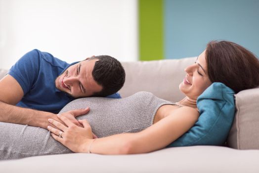 Happy future dad listening the belly of his pregnant wife while relaxing on sofa at home