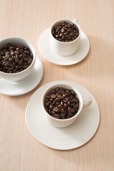 Full coffee beans cups on the wood background