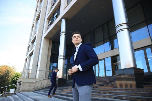 Portrait of a handsome businessman in a suit standing outside a city building.