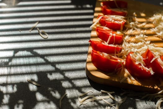 A small pile of grated fresh cheese and red tomatoes lies on a wooden board in the kitchen.