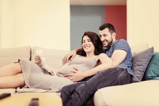 Young pregnant couple looking baby's ultrasound photo while relaxing on sofa at home