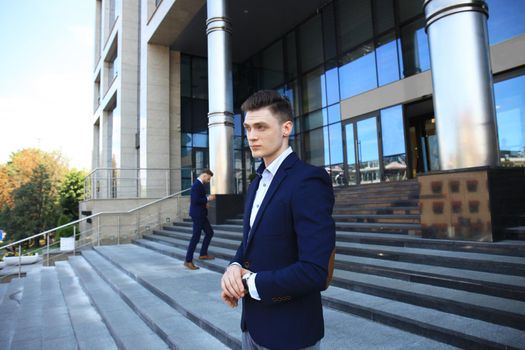 Portrait of a handsome businessman in a suit standing outside a city building.