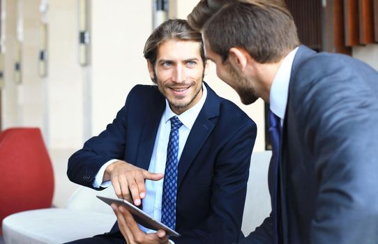 Two young businessmen using touchpad at meeting.