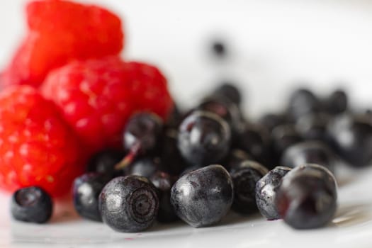 Stock photo close-up of black currant berries isolated on white background and unfocused red raspberries. Different fresh berries on white. Selective focus.