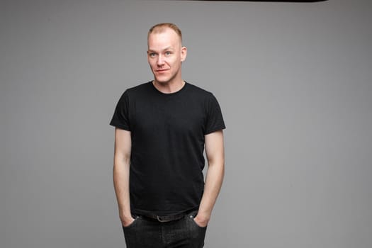picture of attractive male wearing a black t-shirt and jeans poseing for the camera with hands in pockets on grey background