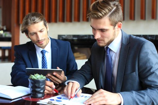 Two young businessmen using touchpad at meeting.
