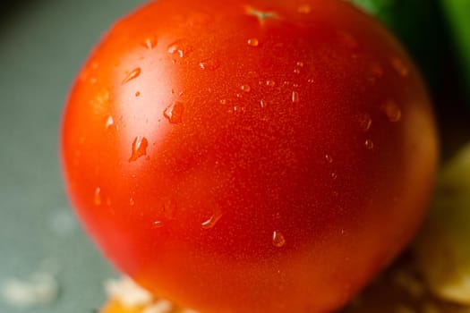 Picture with focus on washed red tomato lies on the table with drops of water on it