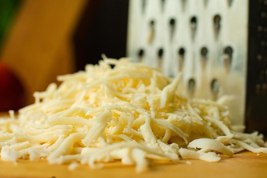 Picture of metal kitchen grater with oval holes on it on the kitchen table with cheese