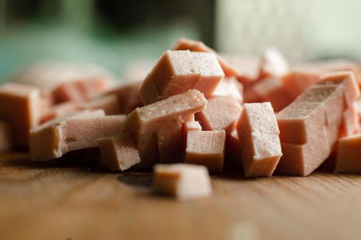 Picture of a small pile of cube sliced sausage for cooking on a wooden table in the kitchen