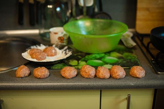 Cooking meatballs, ready mince lies by roasting on the kitchen table in big light kitchen
