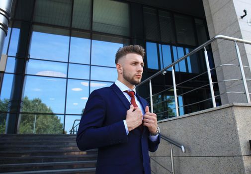 Portrait of a handsome businessman in a suit standing outside a city building.