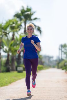 young sporty female runner training for marathon running at beautiful tropical park in the sunny morning