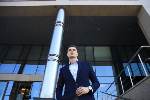 Portrait of a handsome businessman in a suit standing outside a city building.