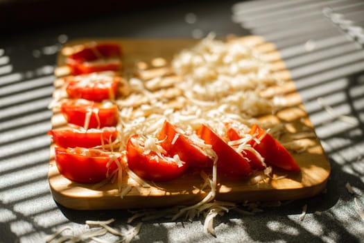 A small pile of grated fresh cheese and red tomatoes lies on a wooden board in the kitchen.