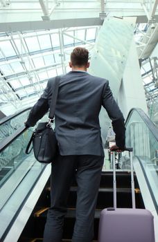 Businessman at the airport going down the escalator.