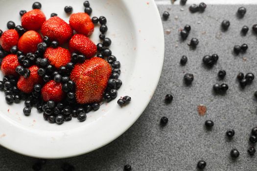 Picture of fresh berries in a white ceramic plate on grey background