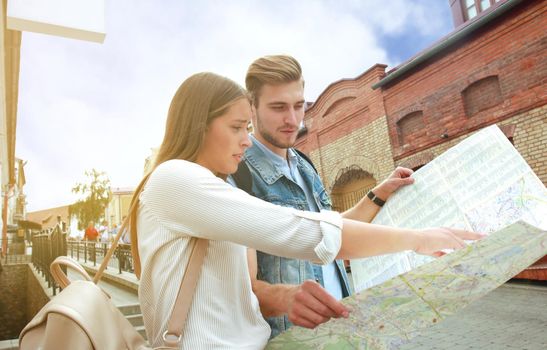 Happy couple walking outdoors sightseeing and holding a map.