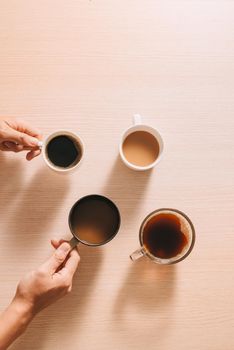 Hands holding cups of coffee on wood background
