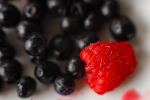 picture of juicy fresh ripe red raspbberries and blueberries in a white ceramic plate with light background