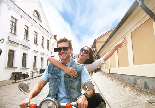 happy young couple riding scooter in town. Handsome guy and young woman travel. Adventure and vacations concept.