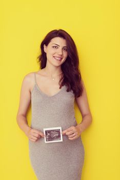 smiling pregnant woman showing ultrasound picture of her unborn baby isolated on yellow background
