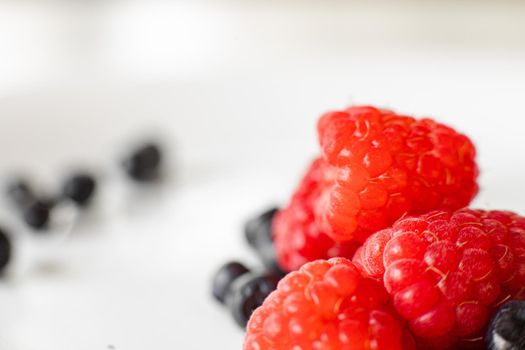 Macro stock photo of fresh, sweet and organic black currant on red ripe raspberries.