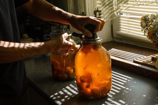 A woman rolls a compote in a large jar under the sun in summer at home in the village.