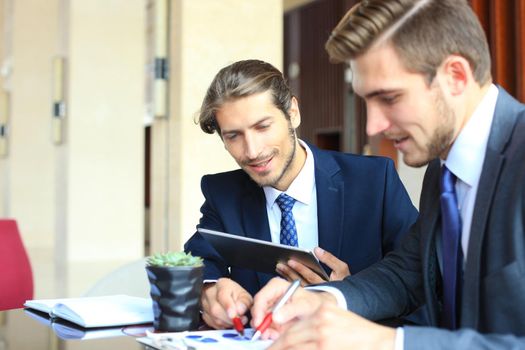 Two young businessmen using touchpad at meeting.