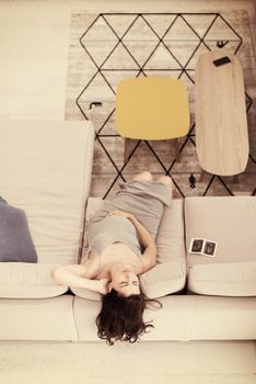 top view of a young pregnant woman looking baby's ultrasound photo while relaxing on sofa at home