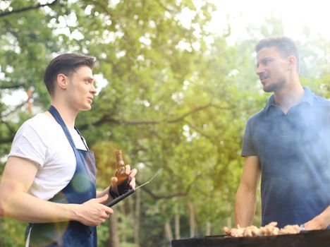 Happy friends grilling meat and enjoying barbecue party outdoors.