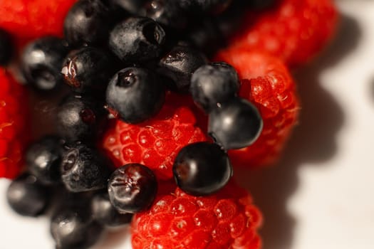 picture of juicy fresh ripe red raspbberries and blueberries in a white ceramic plate with light background