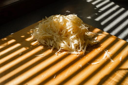 A small pile of grated fresh cheese lies on a wooden board in the kitchen.