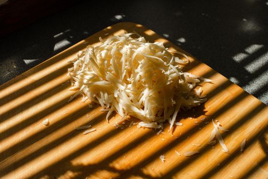 A small pile of grated fresh cheese lies on a wooden board in the kitchen.