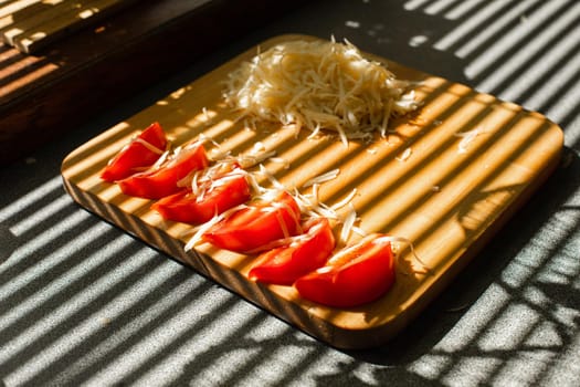 A small pile of grated fresh cheese and red tomatoes lies on a wooden board in the kitchen.