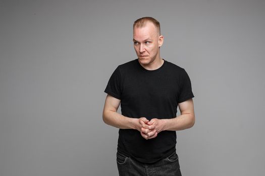 picture of handsome caucasian male keeps hands together looks with surprised sight isolated on grey background