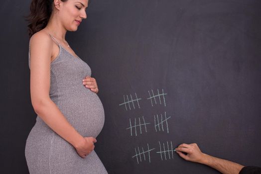 young pregnant couple accounts week of pregnancy and writing them with chalk on blackboard